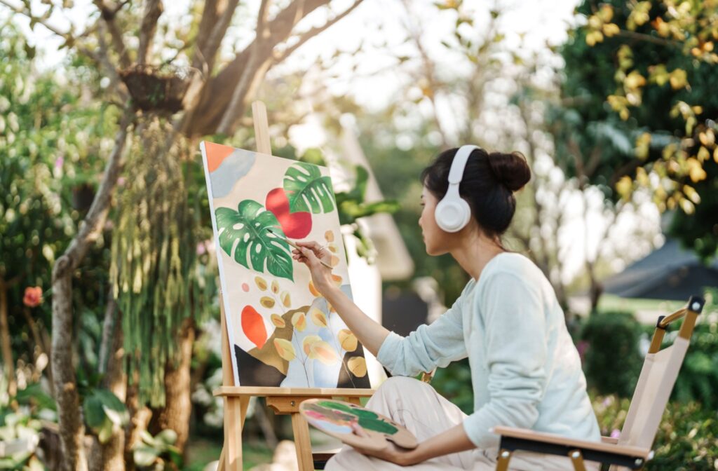 A young woman participates in art and music therapy by painting a picture.