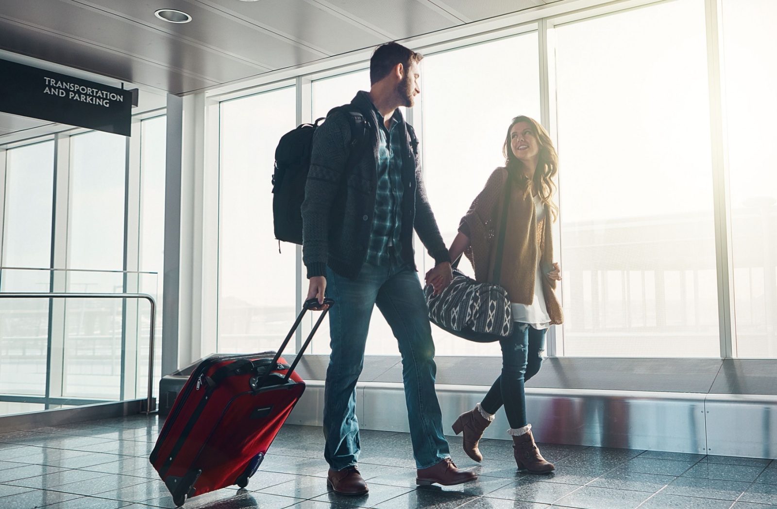 Couple walking through an airport terminal holding hands and carrying luggage for a fresh start for recovery.
