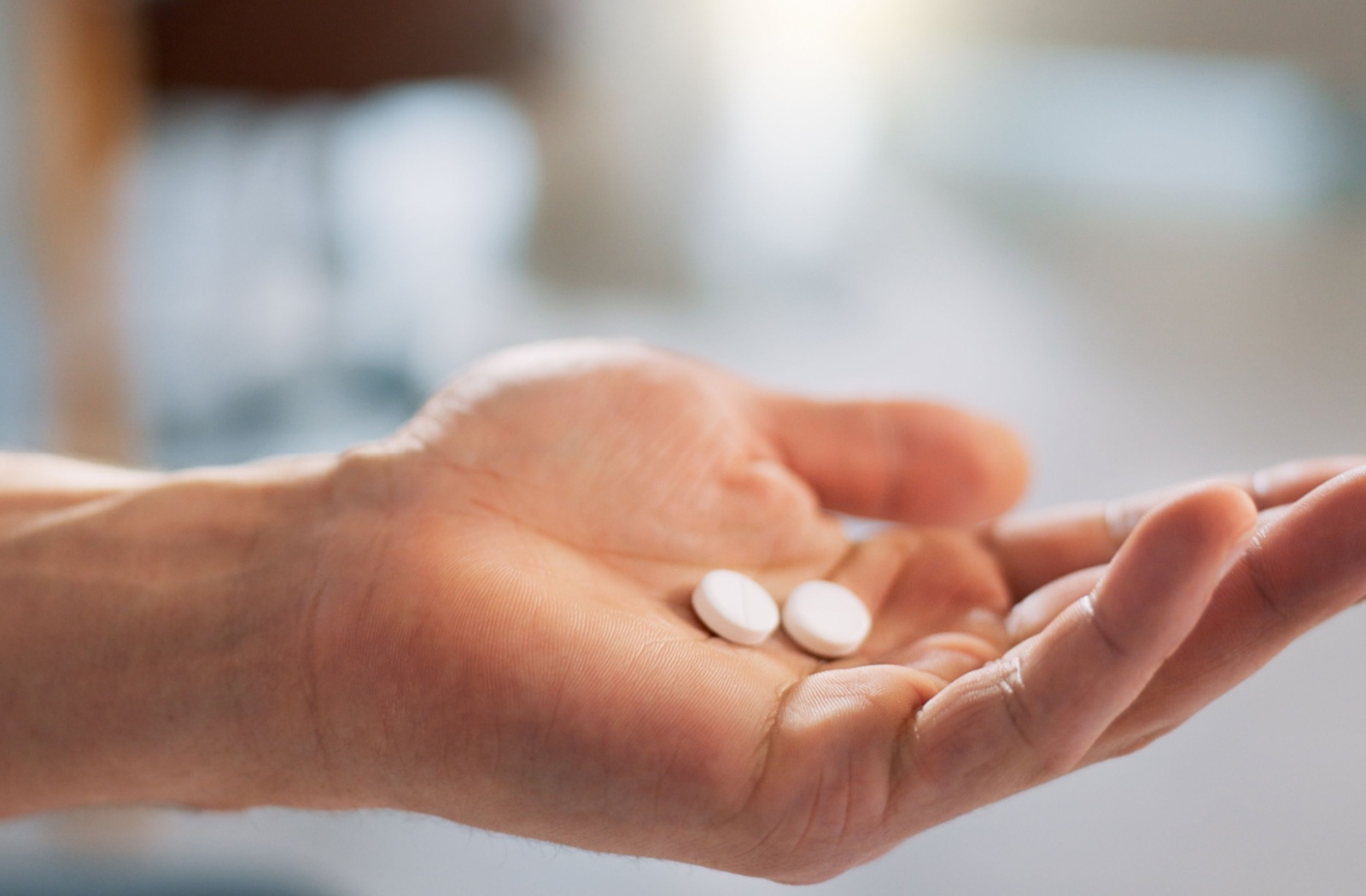 Close-up of a hand holding two medication pills, representing how Medication-Assisted Treatment (MAT) can support patients during detox and rehab.