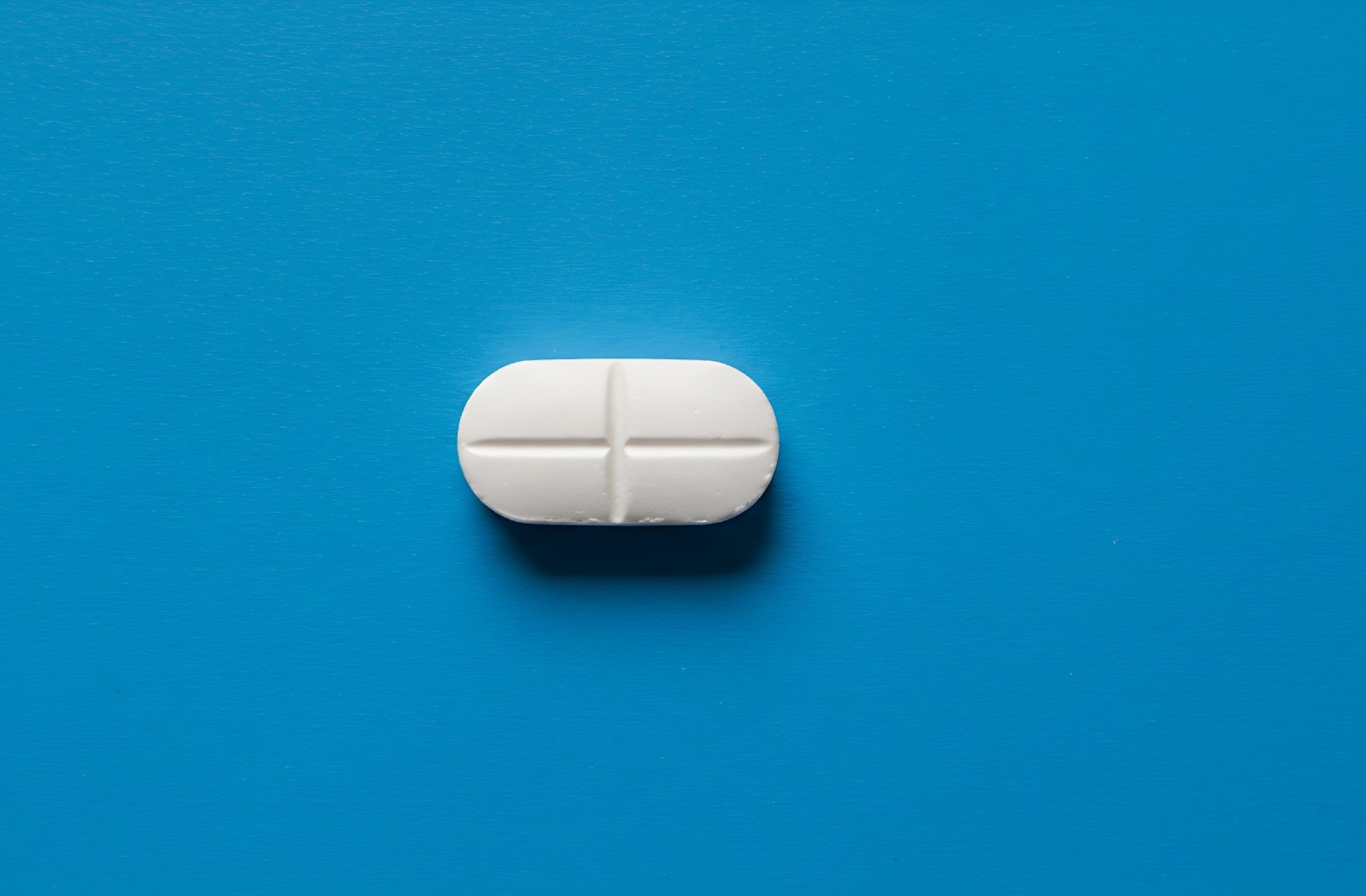 Close-up of a single amino acid supplement capsule on a blue background.