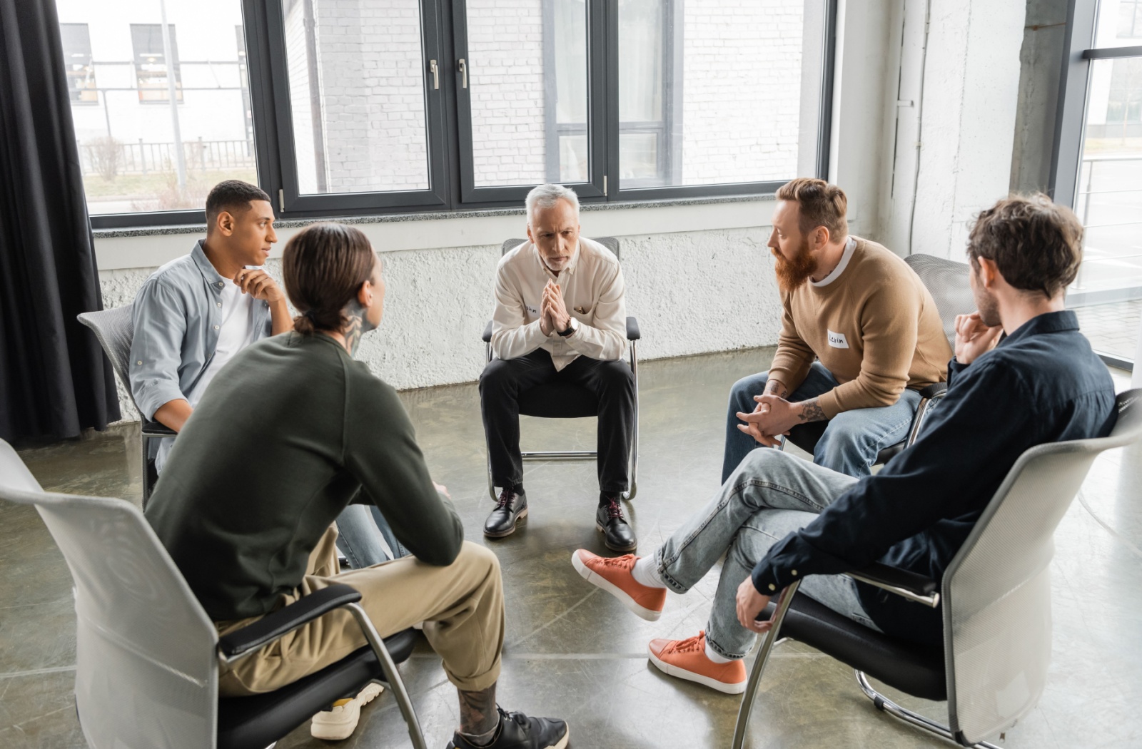 A group of four clients in rehab during a group therapy session, sitting in a circle and talking.