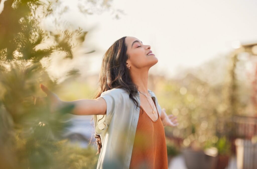 A young woman happily standing in a park with her arms stretched out after beginning her journey with sobriety.