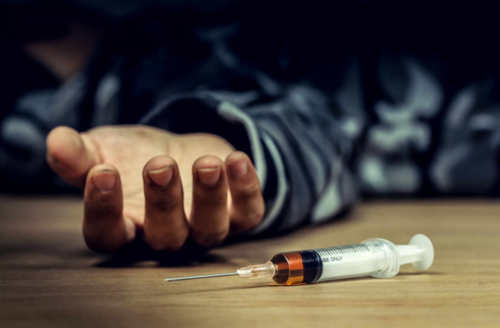 A man lying unconscious after a fentanyl overdose, with a syringe placed next to his hand.