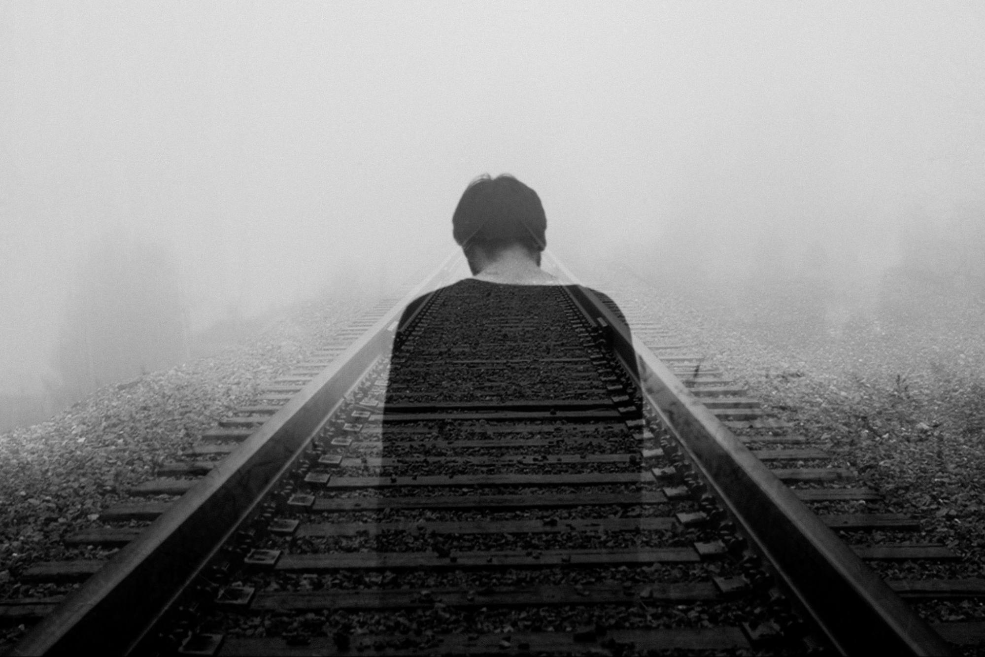 Grayscale photo of a man with a high addiction severity index score fading into train tracks.