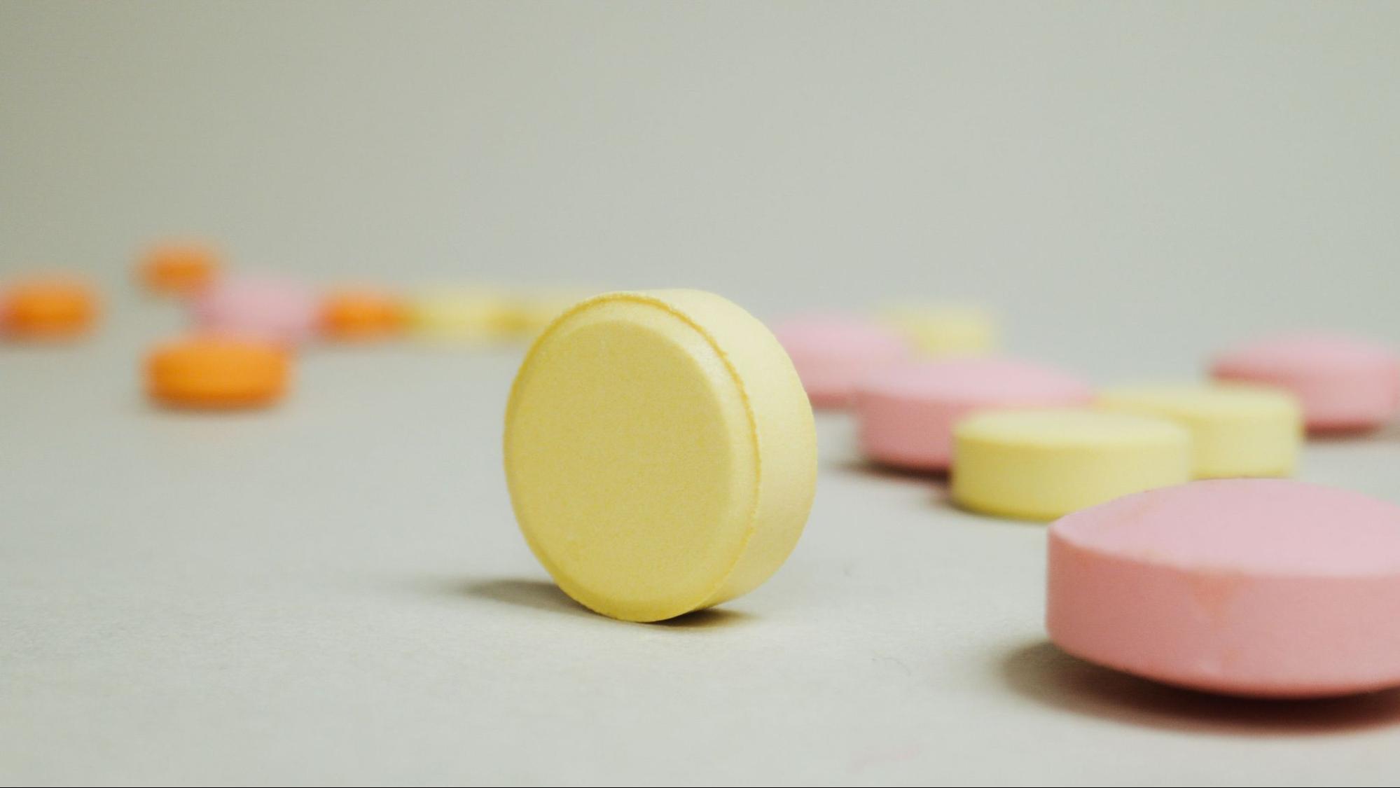 A close-up view of yellow and pink medicinal tablets on a neutral background representing 7-hydroxymitragynine pills.